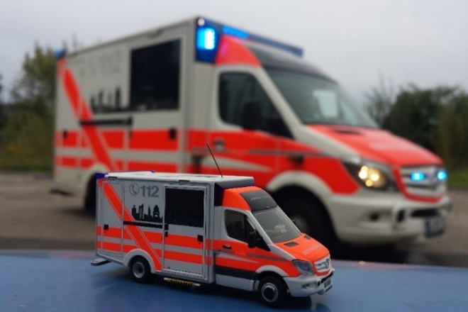 Ein Spielzeug Rettungswagen steht vor einem echten RTW