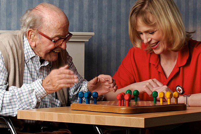 älterer Mann spielt mit Pflegekraft Mensch ärgere dich nicht