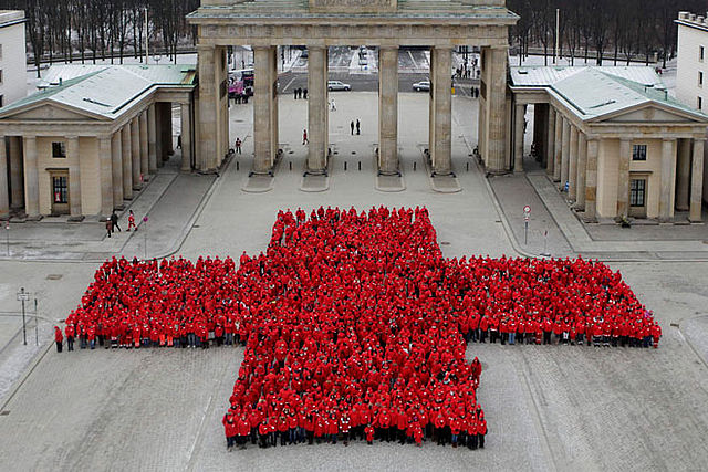 viele Menschen in roter Kleidung formen vor dem Brandenburger Tor ein rotes Kreuz