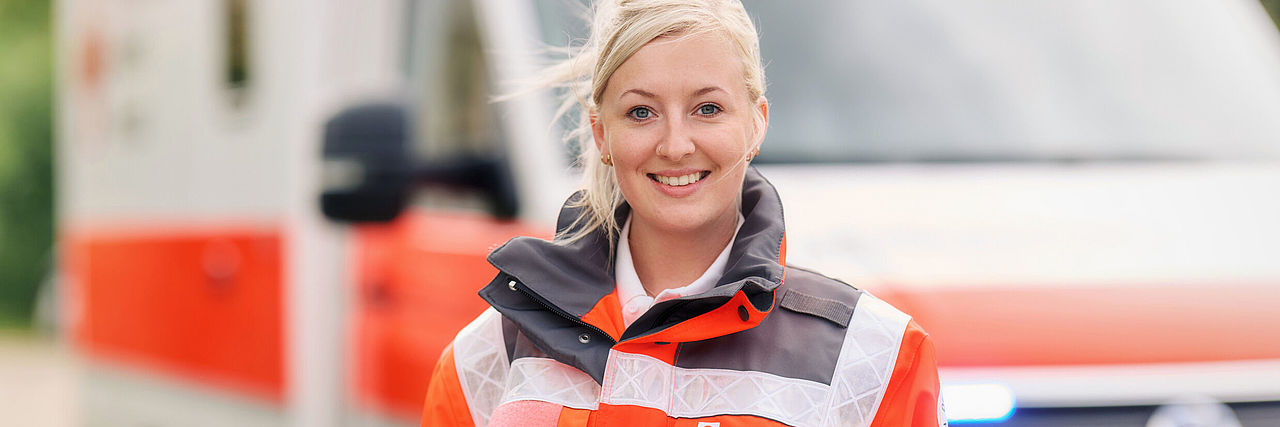 Frau in DRK-Einsatzkleidung steht vor einem Rettungswagen