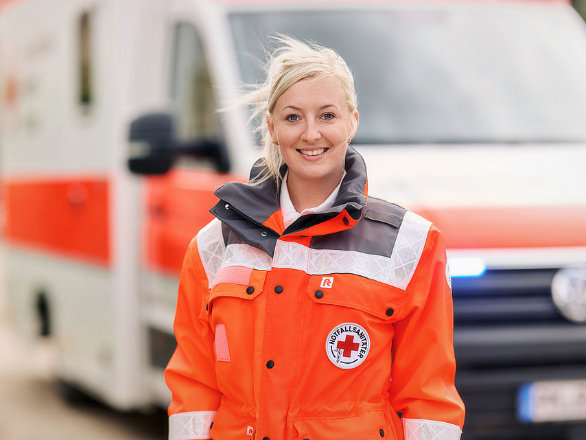 Frau in DRK-Einsatzkleidung steht vor einem Rettungswagen