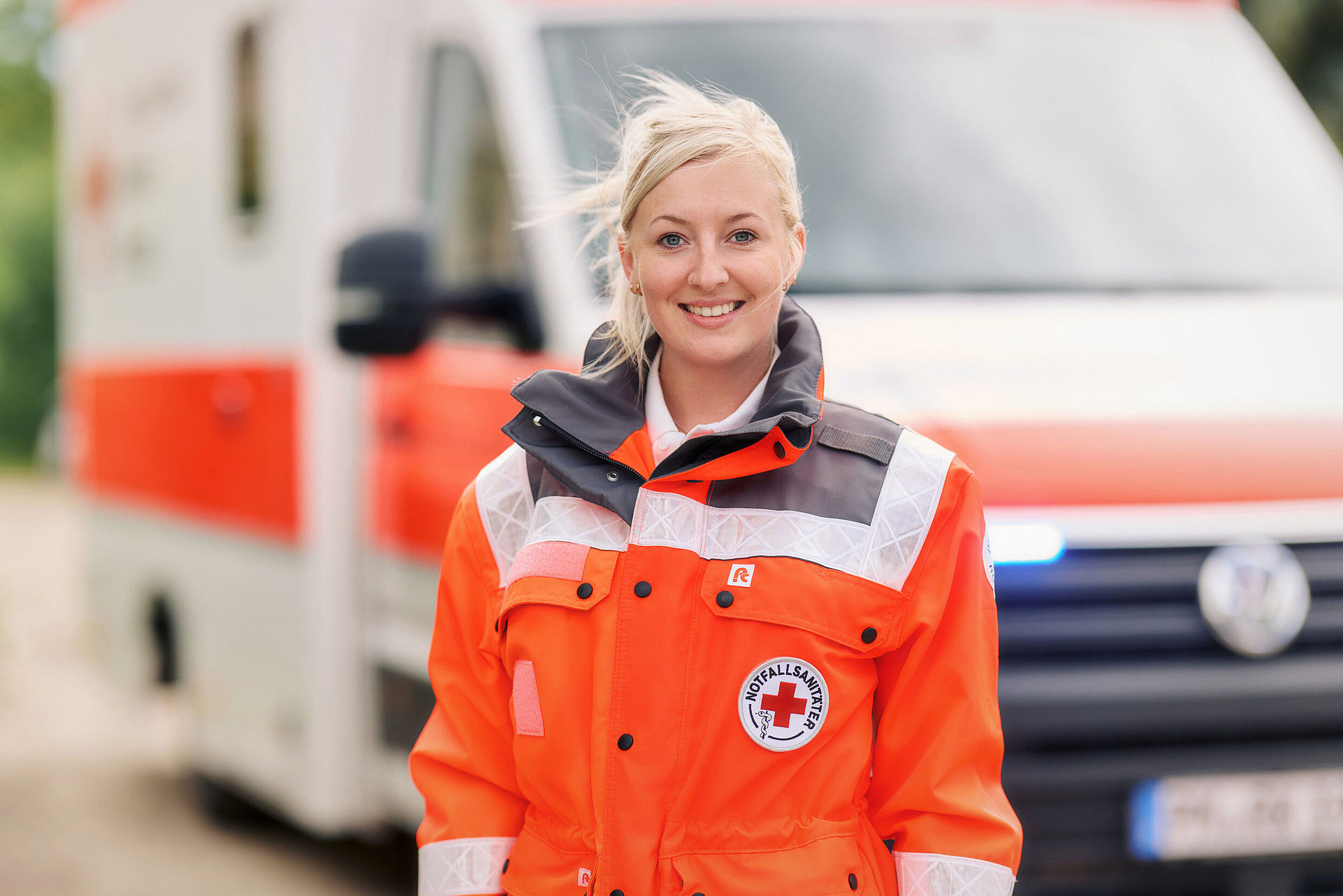 Frau in DRK-Einsatzkleidung steht vor einem Rettungswagen