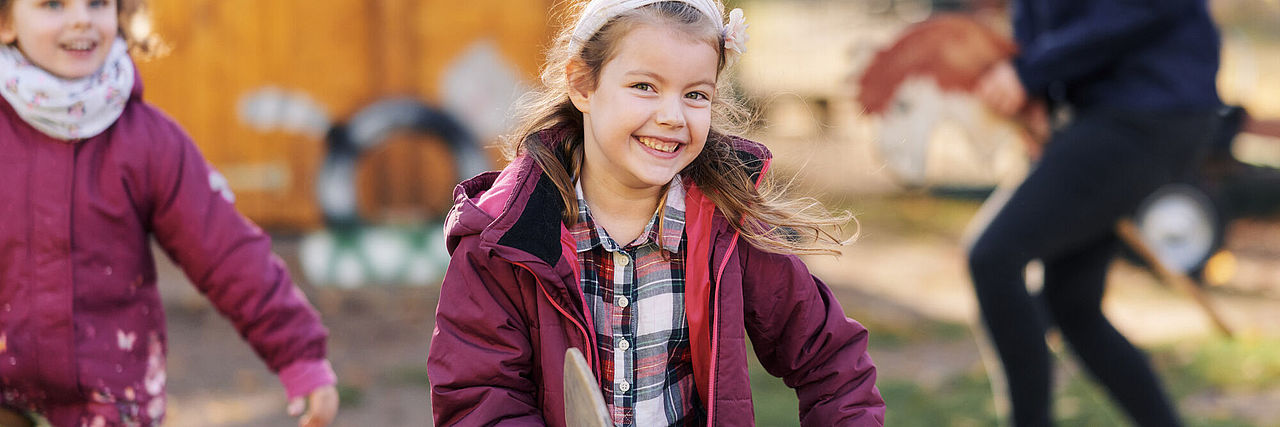 Mädchen rennen lachend durch den Garten, Frau reitet auf Steckenpferd