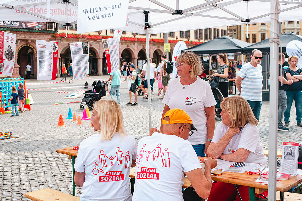 Mehrere Menschen mit T-Shirt "Team Sozial" sitzen auf Bänken
