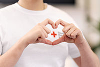 Finger formen ein Herz, DRK-Logo schaut aus dem Herz hervor