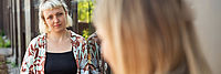 2 Frauen lehnen an einer Hauwand und sprechen miteinander