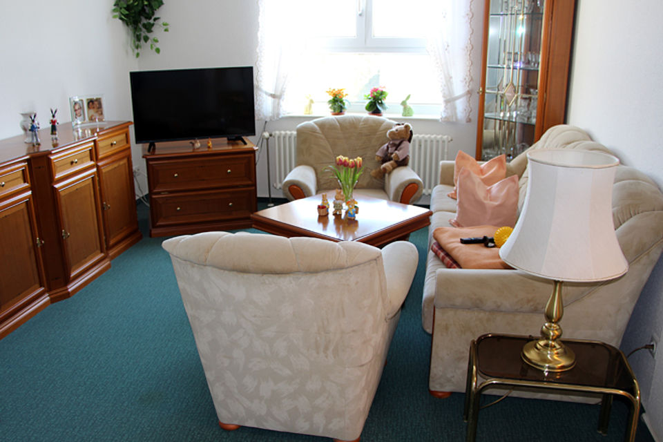 Wohnzimmer, welches mit Sofa, Sesseln, Sideboard, Tisch eingerichtet ist