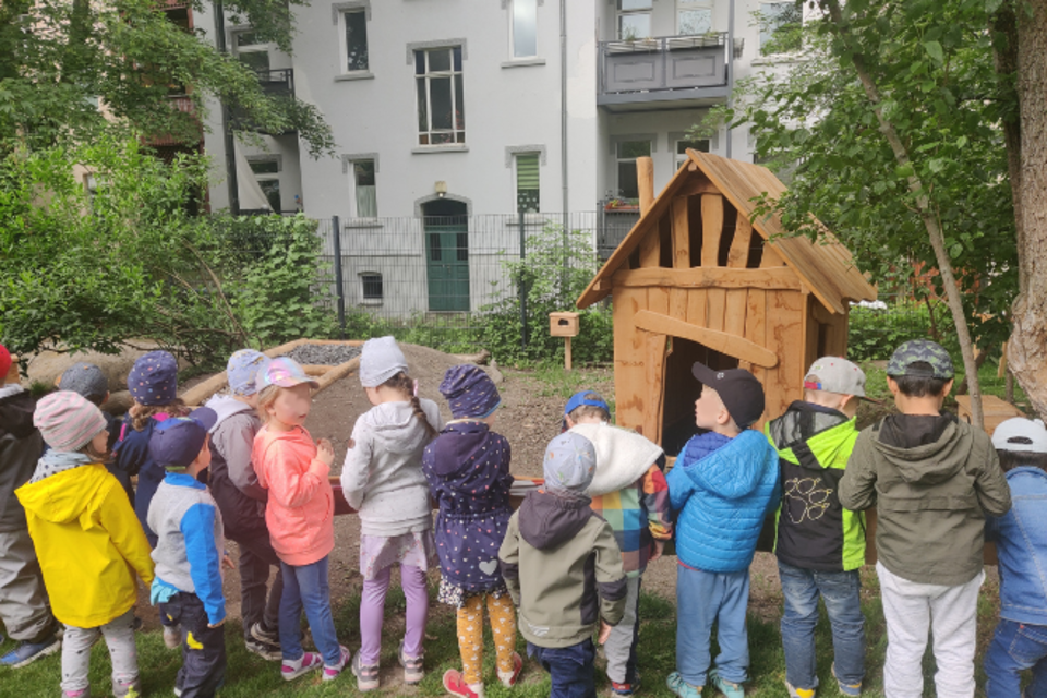 Kinder stehen vor neuem Barfußpfad und neuem Spielhaus im Garten