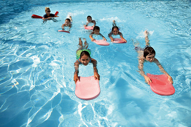 Kinder bewegen sich im Wasser mit Schwimmbrettern fort