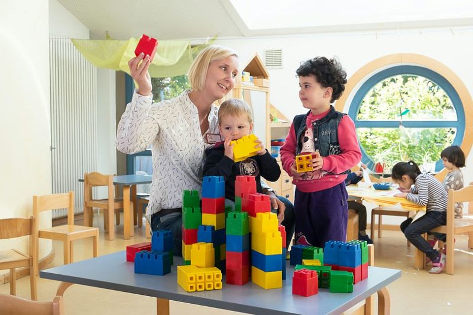 Erzieherin baut mit 2 Kindern Türme aus Platikbausteinen