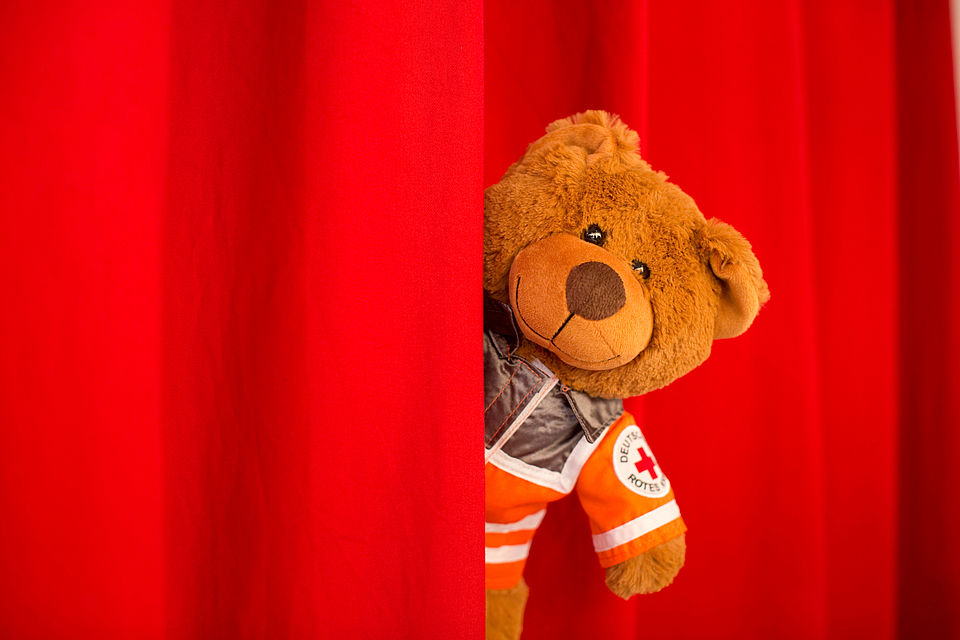 Plüschteddy schaut hinter rotem Vorhang vor