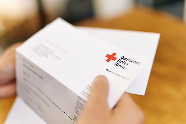Hände halten halb aufgefalteten Brief mit DRK-Logo