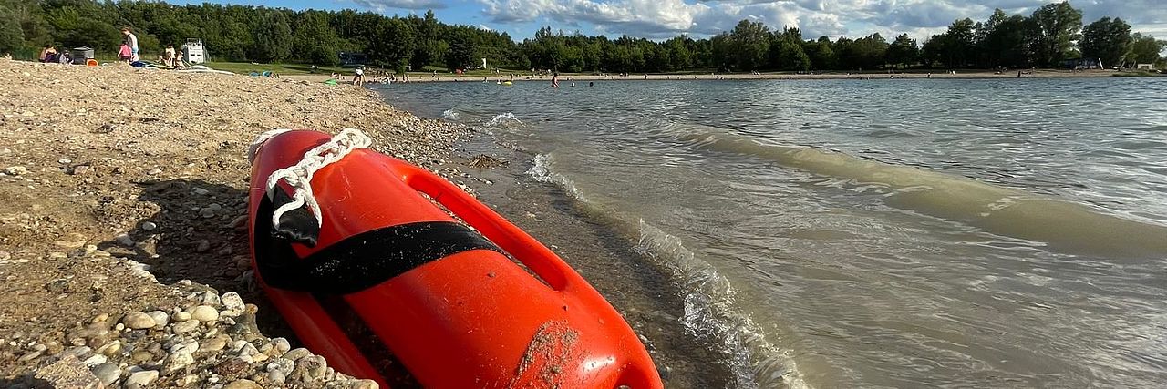 Rettungsboje liegt im Kies am Gewässerrand