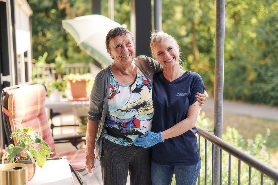 Helferin umarmt ältere Frau, beide lächeln