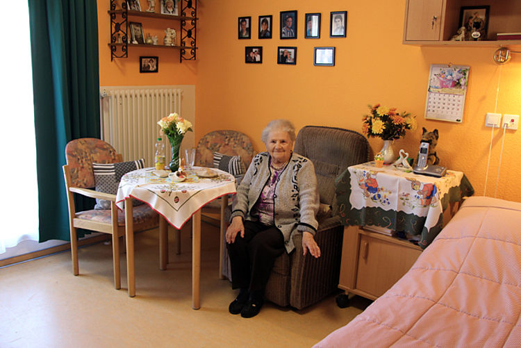 Ältere Dame sitzt in ihrem Zimmer, ausgestattet mit eigenen Möbeln