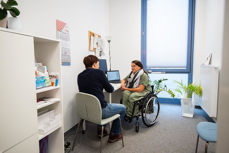 Frau im Rollstuhl unterhält sich mit 2. Person im Büro