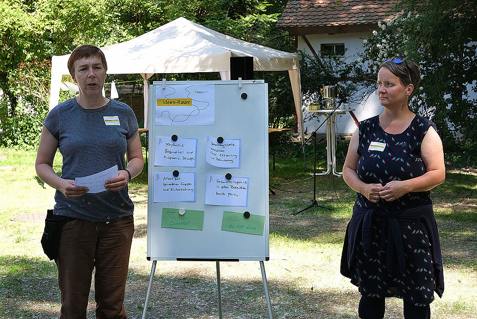 2 Frauen stehen neben einem beschriebenen Flipchart