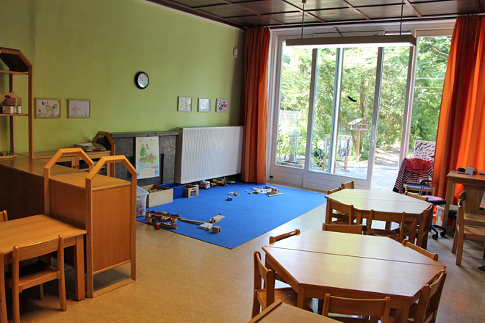 Zimmer mit Tischen, Stühlen, Spielecke und großem Fenster