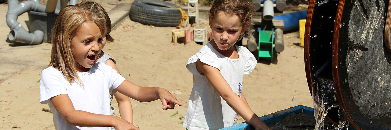 Zwei Kinder spielen im Sandkasten mit Wasser.