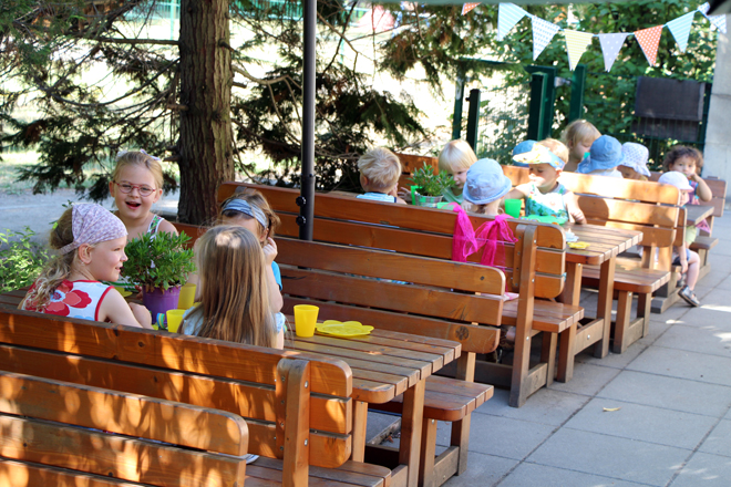 Viele Kinder sitzen auf Bänken der Terrasse "Abenteuerland" und essen kleine Snacks.