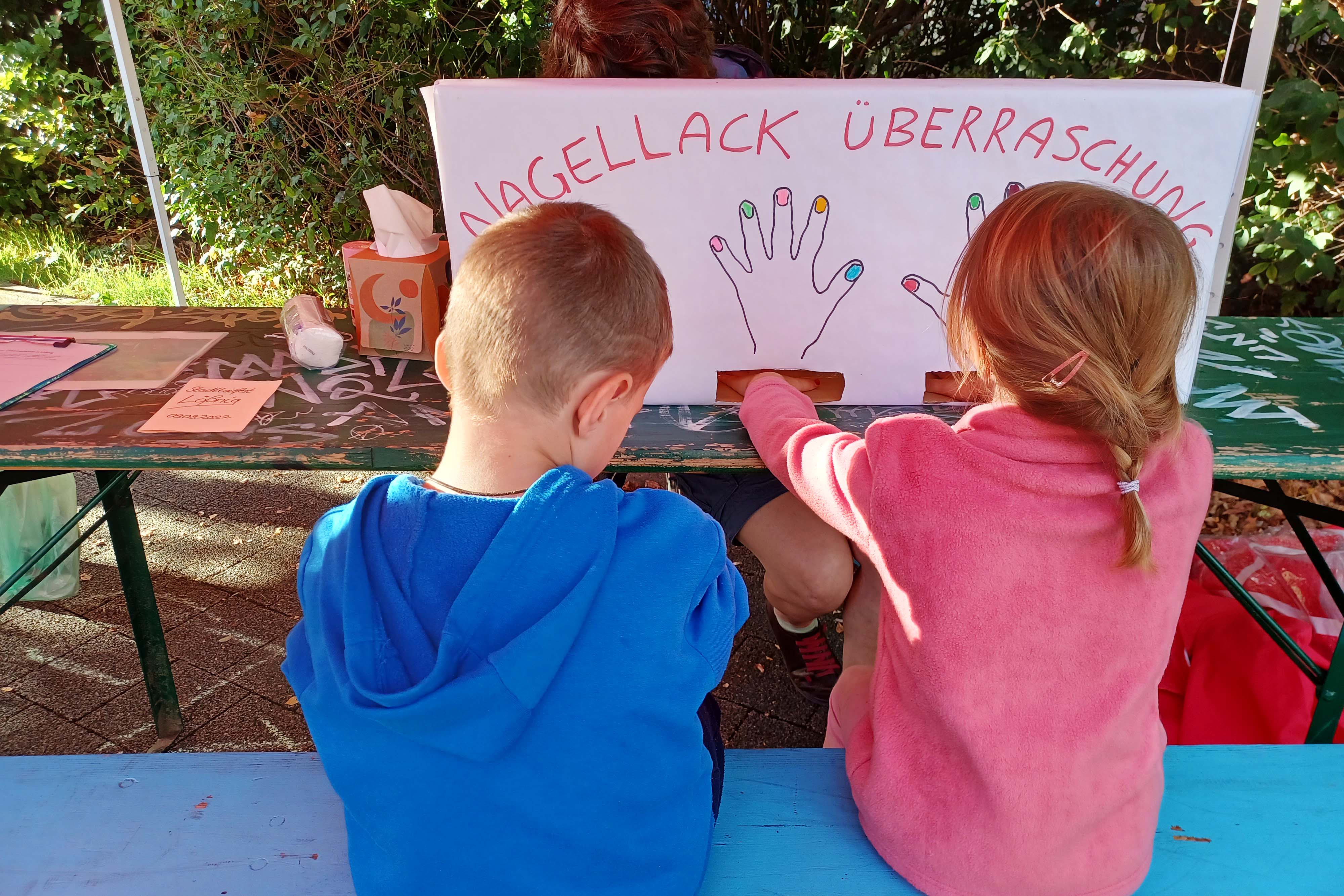 Zwei Kinder sitzen vor einer "Nagellack-Überraschung" und lassen sich die Finger lackieren.